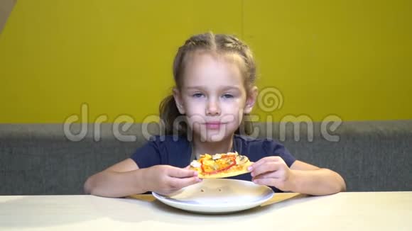 小女孩在有黄色墙壁的咖啡馆里吃披萨的肖像在慢动作中视频的预览图