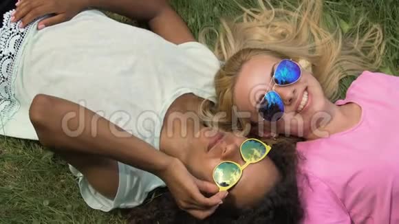 戴墨镜的快乐女孩躺在草地上享受暑假度假视频的预览图