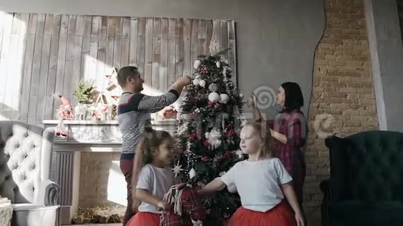 年轻的父母装饰圣诞树他们的双胞胎女儿骑玩具马新年快乐圣诞节快乐视频的预览图