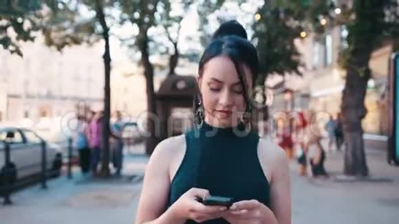 自信迷人的蓝眼睛黑发女人穿着时尚的服装走在市中心的一条街上用她手机视频的预览图
