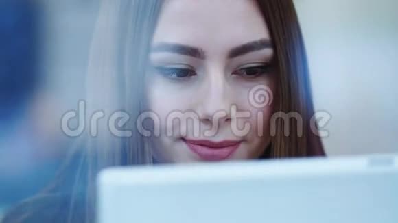 在外面拍摄一个快乐的美女她的脸坐在一家咖啡馆的窗前用平板电脑微笑着视频的预览图