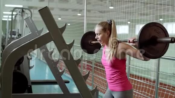 金发女郎做仰卧起坐肩膀上戴着杠铃一个漂亮的女孩正在健身房锻炼视频的预览图