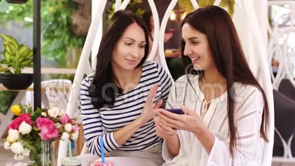 两个漂亮的女孩在看着坐在咖啡馆里的手机照片时笑了视频的预览图