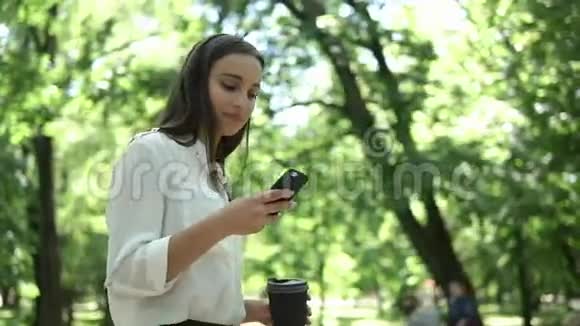女人在公园里用咖啡检查她的手机视频的预览图