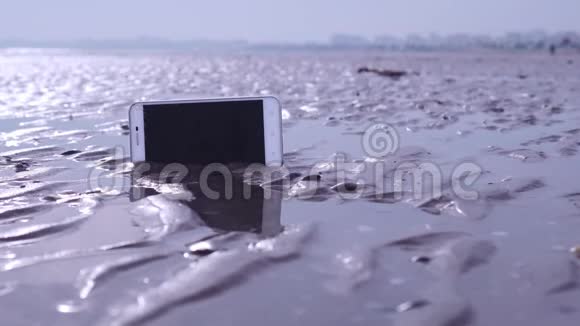 智能手机卡在海滩的潮湿沙滩上视频的预览图