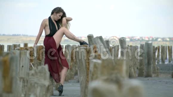 一位身穿连衣裙的金发美女在河口中部的木柱上踩着废弃的盐视频的预览图