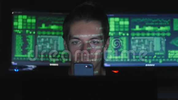 黑客程序员使用智能手机而绿色代码字符反映在他的脸在黑暗的办公室房间视频的预览图