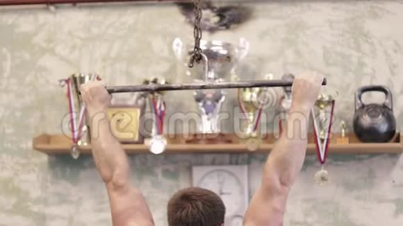 在健身房进行交叉训练时赤膊运动员在酒吧里做仰卧起坐视频的预览图