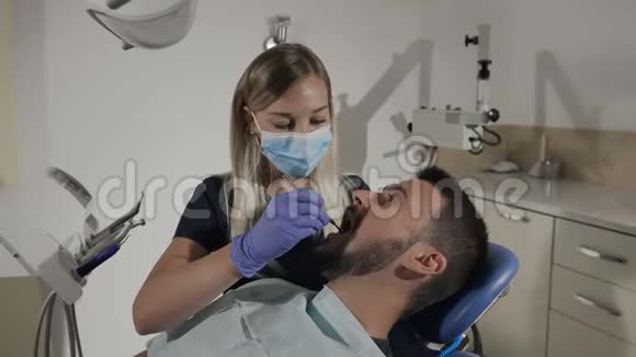 女牙医用口腔镜和牙科挖掘机检查病人牙齿视频的预览图