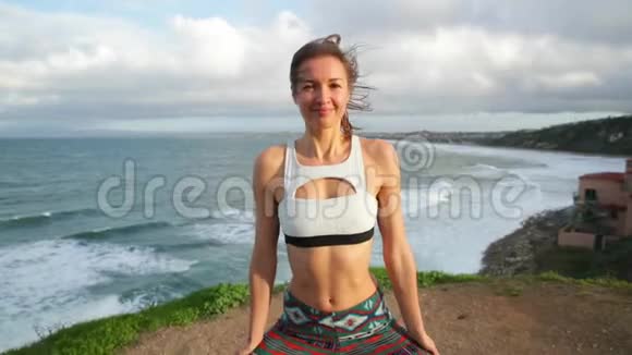 年轻女子在黎明或日落时在岩石上靠近海洋练习瑜伽相机旋转360度视频的预览图