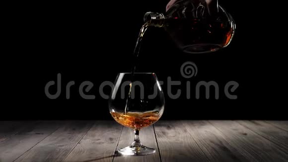 豪华白兰地手把金白兰地从一个圆形的瓶子里倒入一个玻璃在木桌上的黑色背景白兰地白兰地视频的预览图