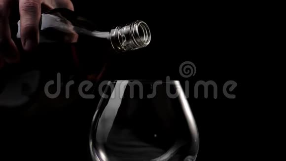 豪华白兰地手把金白兰地从一个圆形的瓶子里倒入一个黑色背景的杯子里白兰地白兰地嗅探器狂欢视频的预览图