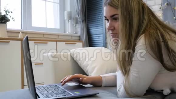 年轻的女人有智能手机和笔记本电脑躺在家里的沙发上视频的预览图