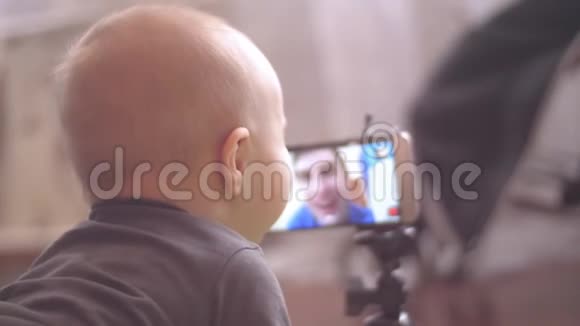 小男孩用智能手机看着Skype上的白人爸爸触摸屏幕4K室内后景特写视频的预览图