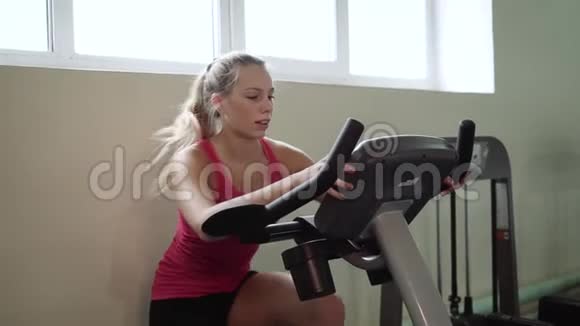 年轻漂亮的女孩在健身房里在自行车模拟器上摇晃着她的腿理念热爱运动去健身房适当的视频的预览图