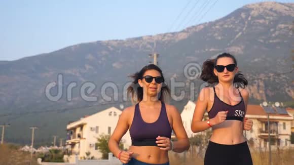 两个年轻女孩在户外跑步和交谈年轻的运动女性在乡间路慢跑女运动员训练视频的预览图