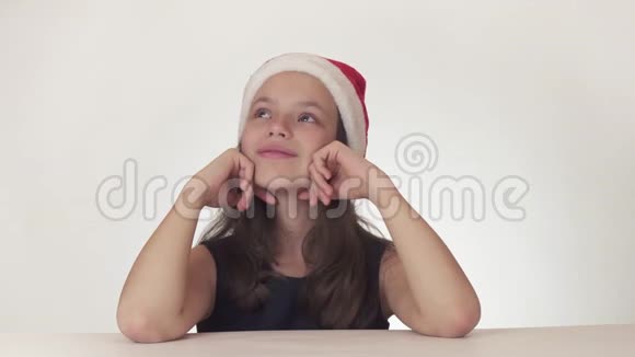 戴着圣诞老人帽的美丽快乐少女在白色背景的股票视频中快乐地做梦和唱歌视频的预览图