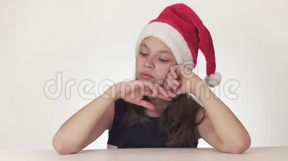 戴着圣诞老人帽子的美丽不幸的少女在白色背景的股票上表达出忧郁的情绪视频的预览图
