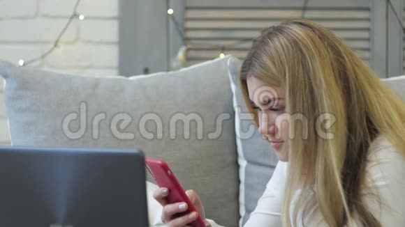 年轻的女人有智能手机和笔记本电脑躺在家里的沙发上视频的预览图