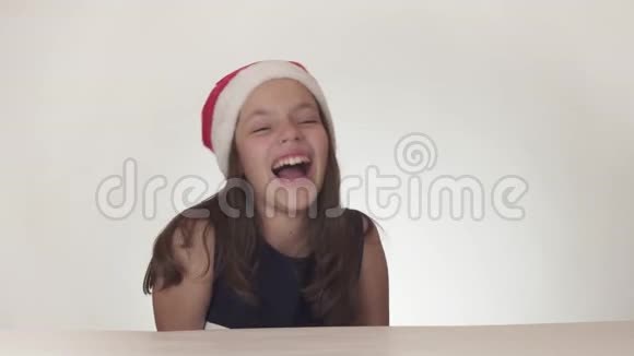 美丽淘气的少女戴着圣诞老人的帽子在白色背景的股票视频中有感情地唱歌视频的预览图