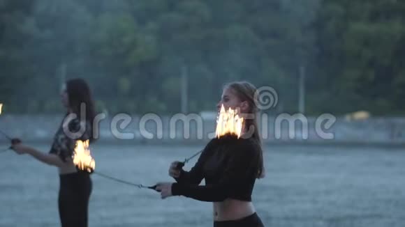 两个年轻女子站在河岸上表演火焰球熟练的火技艺术家表现出娴熟的技巧视频的预览图