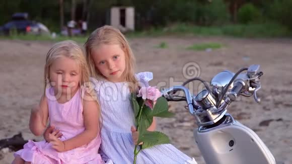 两个金发的小女孩在海滩上为相机摆好姿势两个小妹妹和一朵粉红色的花坐在一起视频的预览图