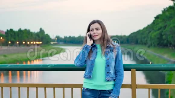 穿着棉袄站在河上的桥上用智能手机说话的漂亮女孩视频的预览图