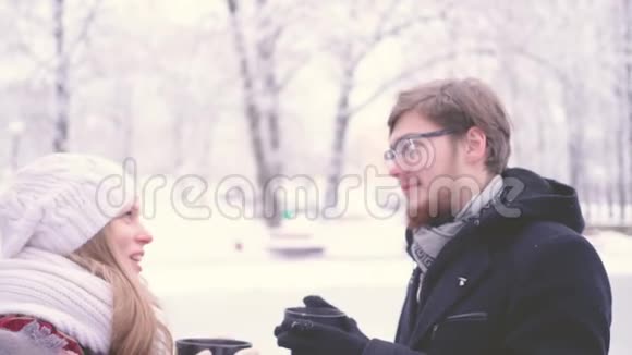 美丽的女孩和男人在冬天的公园里站着手里拿着一杯热可可4K视频的预览图