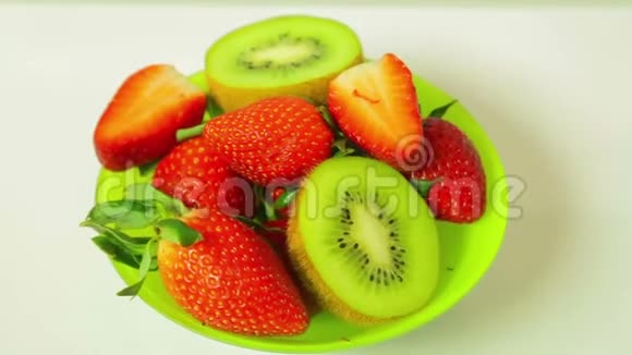 鲜奇异果和切片草莓在蓝色背景上的盘子旋转成一个圆圈从上面看视频的预览图