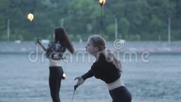 两个年轻女子站在河岸上表演火焰球熟练的火技艺术家表现出娴熟的技巧视频的预览图