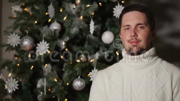成年帅哥站在装饰好的圣诞树旁微笑视频的预览图