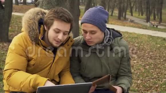 两个朋友的学生在户外使用笔记本电脑和平板电脑视频的预览图