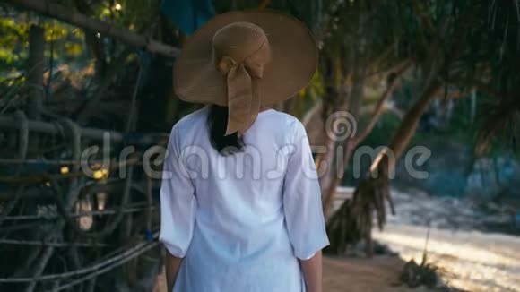 一个戴帽子的孤独女孩正沿着岛屿海岸线散步日出时热带天堂海滩视频的预览图