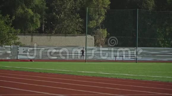 在远处一名运动员沿着跑道跑过一个绿色的足球场视频的预览图