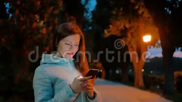 晚上公园里漂亮的女孩用智能手机视频的预览图