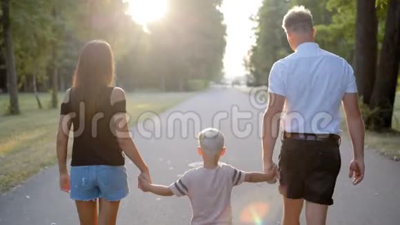 幸福的年轻家庭走在公园里牵着小儿子的手视频的预览图