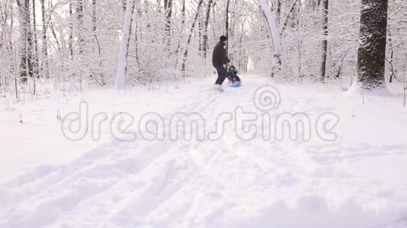 年轻的爸爸在冬天把他的小儿子卷在雪橇上视频的预览图