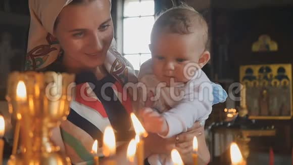 年轻的母亲带着孩子慢慢地观察教堂里燃烧的蜡烛视频的预览图