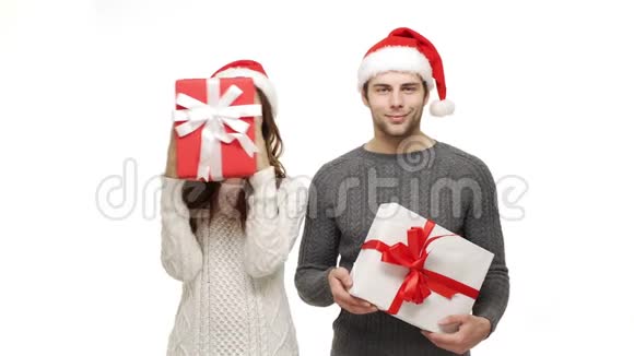 年轻夫妇在白色孤立的背景下玩并躲在圣诞礼物盒后面视频的预览图