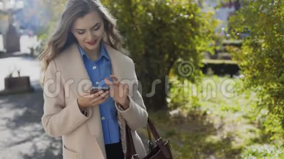 穿着白色外套的漂亮女孩用智能手机视频的预览图
