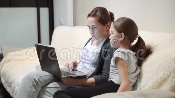 有女儿的女人坐在沙发上用笔记本电脑视频的预览图