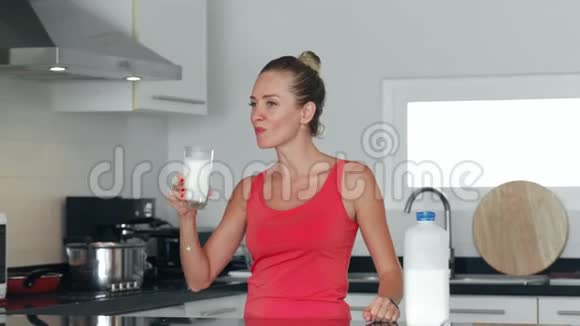 健康的女人从厨房的玻璃杯里喝牛奶把牛奶瓶放冰箱里视频的预览图