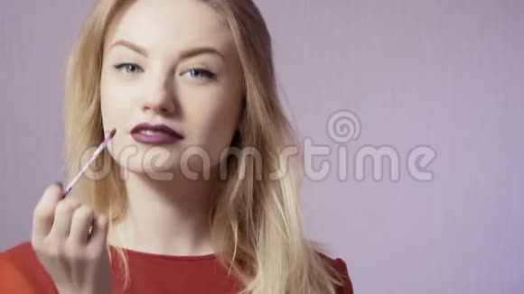美丽的女孩把嘴唇涂成紫色的唇彩视频的预览图