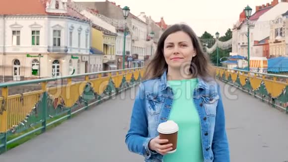穿着棉袄走在人行桥上喝咖啡的漂亮女孩旧城的背景视频的预览图