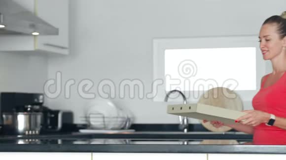 微笑的女人打开披萨盒嗅着厨房里诱人的香气视频的预览图