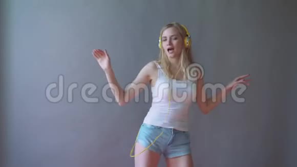 灰色背景的年轻美女听着耳机里的音乐跳舞视频的预览图