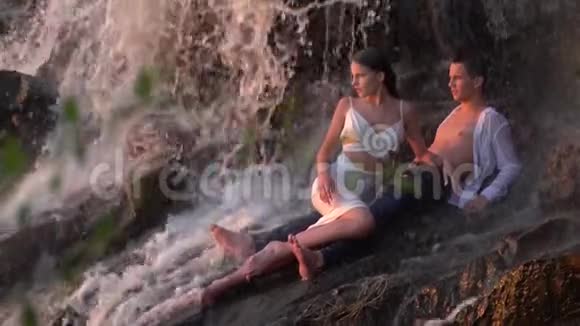一个男人和一个女孩躺在瀑布下看着日落慢动作视频的预览图