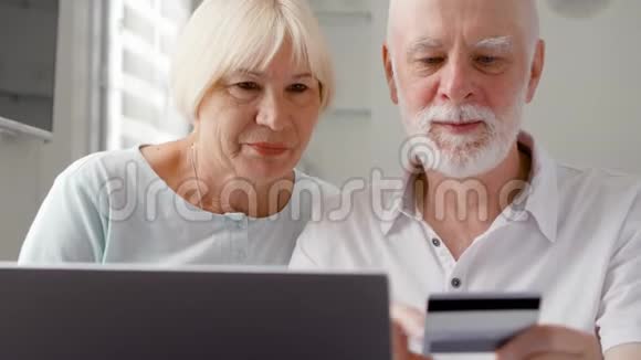 家里的老夫妇用笔记本电脑上的信用卡在线购物退休后积极的现代生活视频的预览图