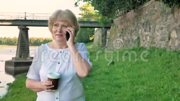 老年妇女沿着海滨散步用智能手机交谈喝咖啡野桥和老墙视频的预览图