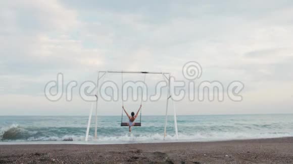 快乐的年轻女子穿着白色泳衣骑在秋千上享受海景假期概念视频的预览图